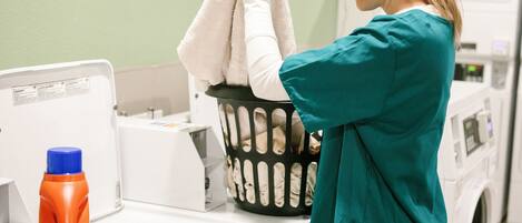 A person in teal scrubs hanging a white towel in a laundry basket on a white washing machine.