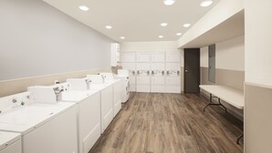 Sala de bugaderia amb diverses rentadores i assecadores, sòl de fusta i una banca.