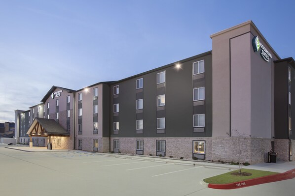 A modern hotel with multiple floors, a well-lit entrance, and a parking area. - WoodSpring Suites West Monroe I-20 (West Monroe)