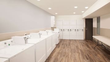 A laundry room with multiple washing machines and dryers, a bench, and a door leading to another area.