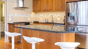 A modern kitchen with wooden cabinets, a stainless steel refrigerator, and a central island with bar stools.