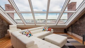 A modern loft apartment with a large white sectional sofa, a patterned rug, and a view through skylights.