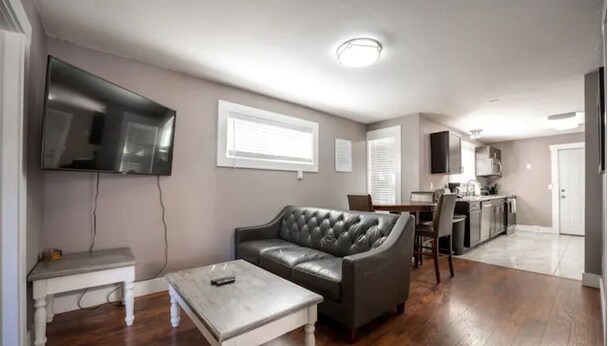 A living room with a leather sofa, a coffee table, a TV mounted on the wall, a dining area with a table and chairs, and a kitchen in the background. - Elegant Tacoma condo unit in downtown B (Tacoma)