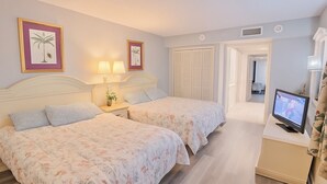 Ein Hotelzimmer mit zwei Betten, einem Fernseher auf einem Nachttisch und einer Tür zu einem Badezimmer.
