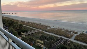 Blick auf einen Strand mit einer hölzernen Steg, der ins Meer ragt, sowie ein Sandstrand und eine Promenade mit Holzkonstruktionen.