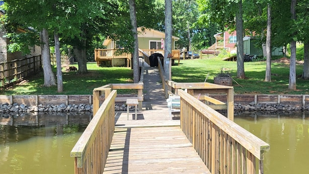 A wooden dock leading to a house with a covered porch, surrounded by trees and a small pond. - Charming Lakefront Retreat: Your Perfect Waterfront Getaway (Lexington)