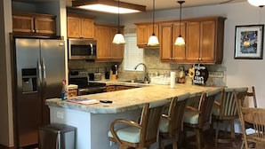 A kitchen with a central island, wooden bar stools, a stainless steel refrigerator, and a microwave. - Charming Lakefront Retreat: Your Perfect Waterfront Getaway (Lexington)