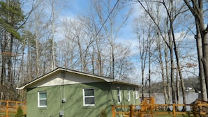 A small, single-story house with a green exterior, a fenced yard, and a wooden deck. - Charming Lakefront Retreat: Your Perfect Waterfront Getaway (Lexington)