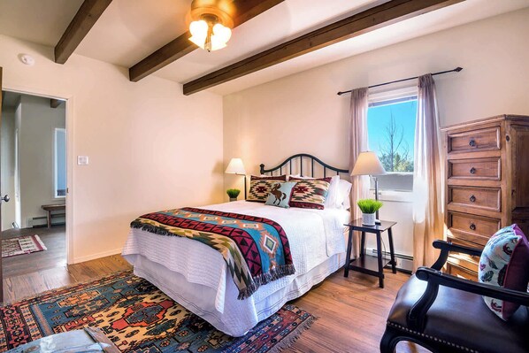 A bedroom with a bed, bedside lamps, a dresser, a window with curtains, and a patterned rug.
