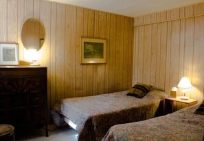 A room with two single beds, wooden paneling on the walls, a dresser, a mirror, and a framed picture. - Mountain View Chalet (Indian Lake)
