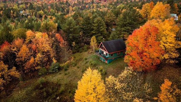 A cabin surrounded by autumn foliage, set in a forested area with a mountainous backdrop. - Mountain View Chalet (Indian Lake)
