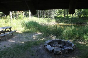 A picnic table and a stone fire pit in a forested area. - Mountain View Chalet (Indian Lake)