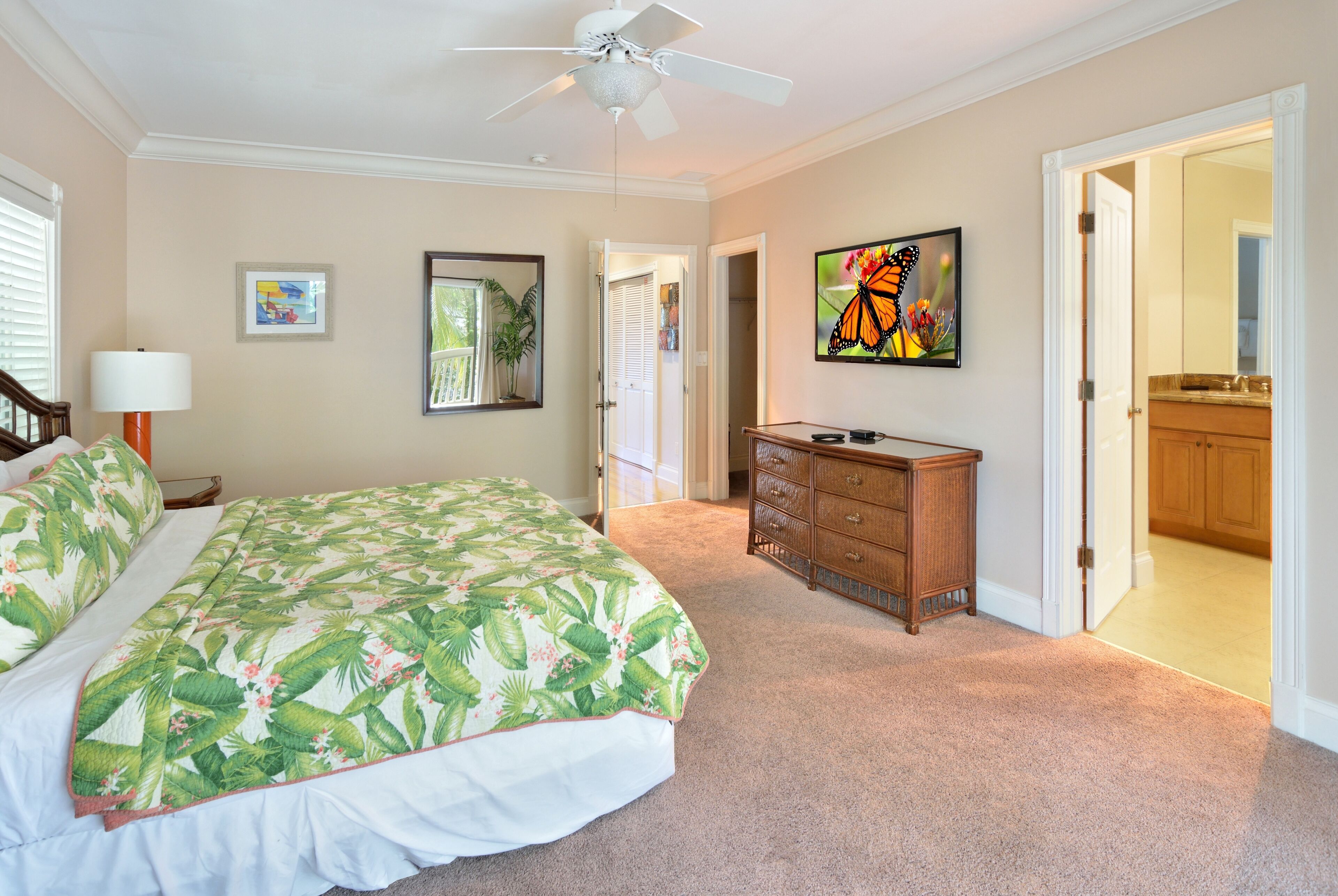 A bedroom with a bed, a ceiling fan, a dresser, and a door leading to another room.