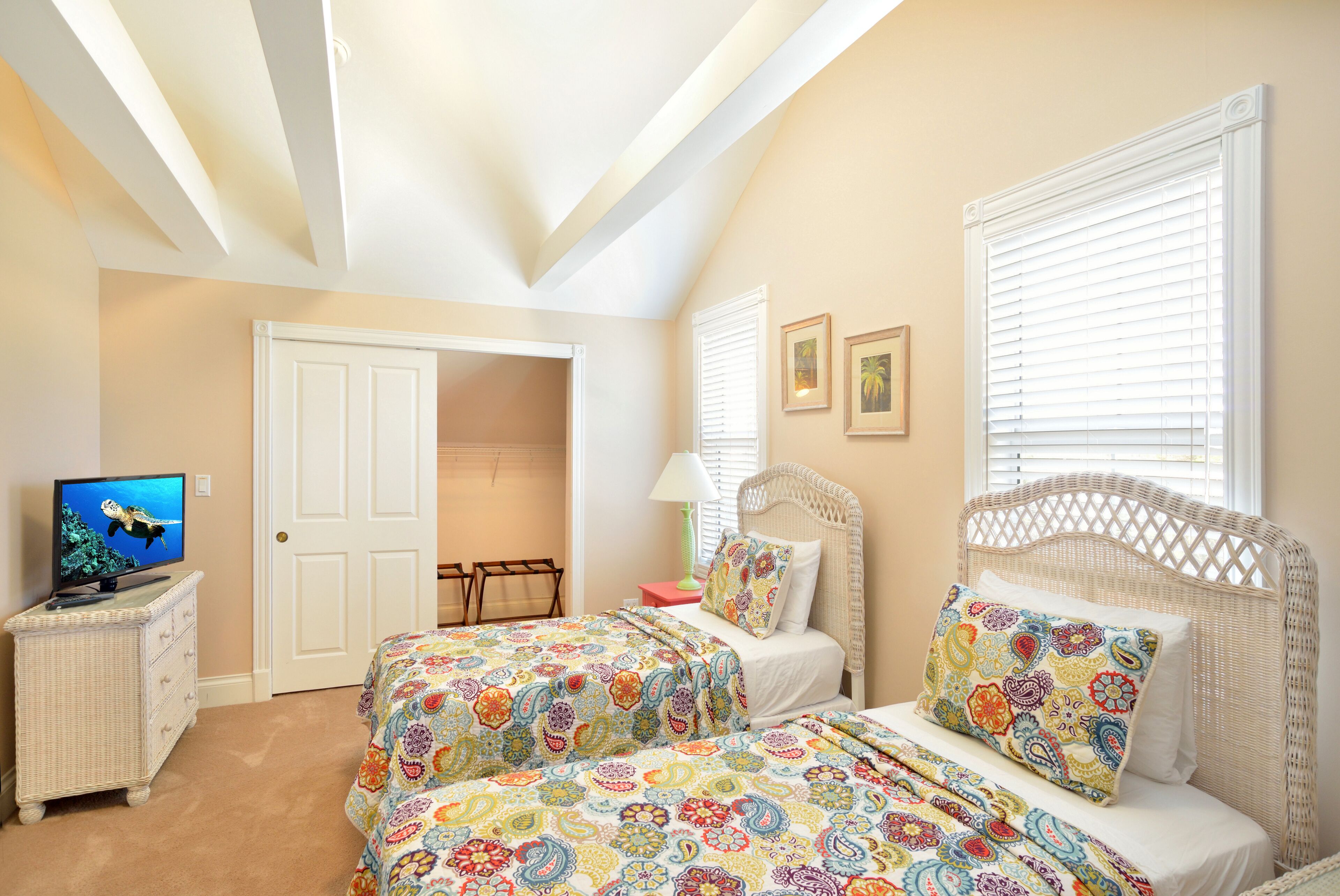 A bedroom with two beds, a television, a dresser, and a door leading to another room.