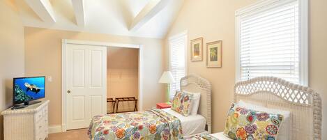 A bedroom with two beds, a television, a dresser, and a door leading to another room.