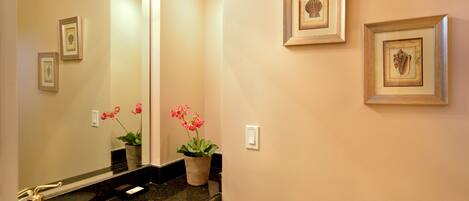 A bathroom with a sink, mirror, framed pictures on the wall, and a potted plant.