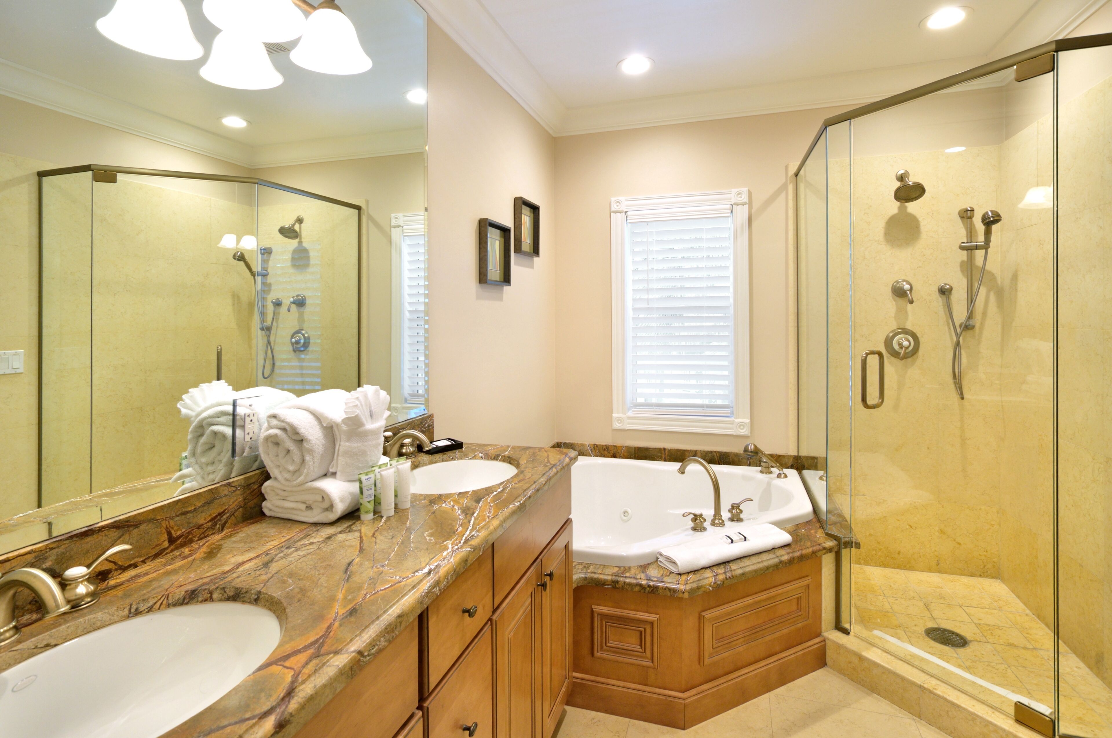 A bathroom with two sinks, a large mirror, a glass-enclosed shower, and a vanity with marble countertops.
