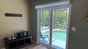 Una habitación con piso de madera, un mueble multimedia oscuro, un perchero y un ventanal corredero que da a una zona de piscina.