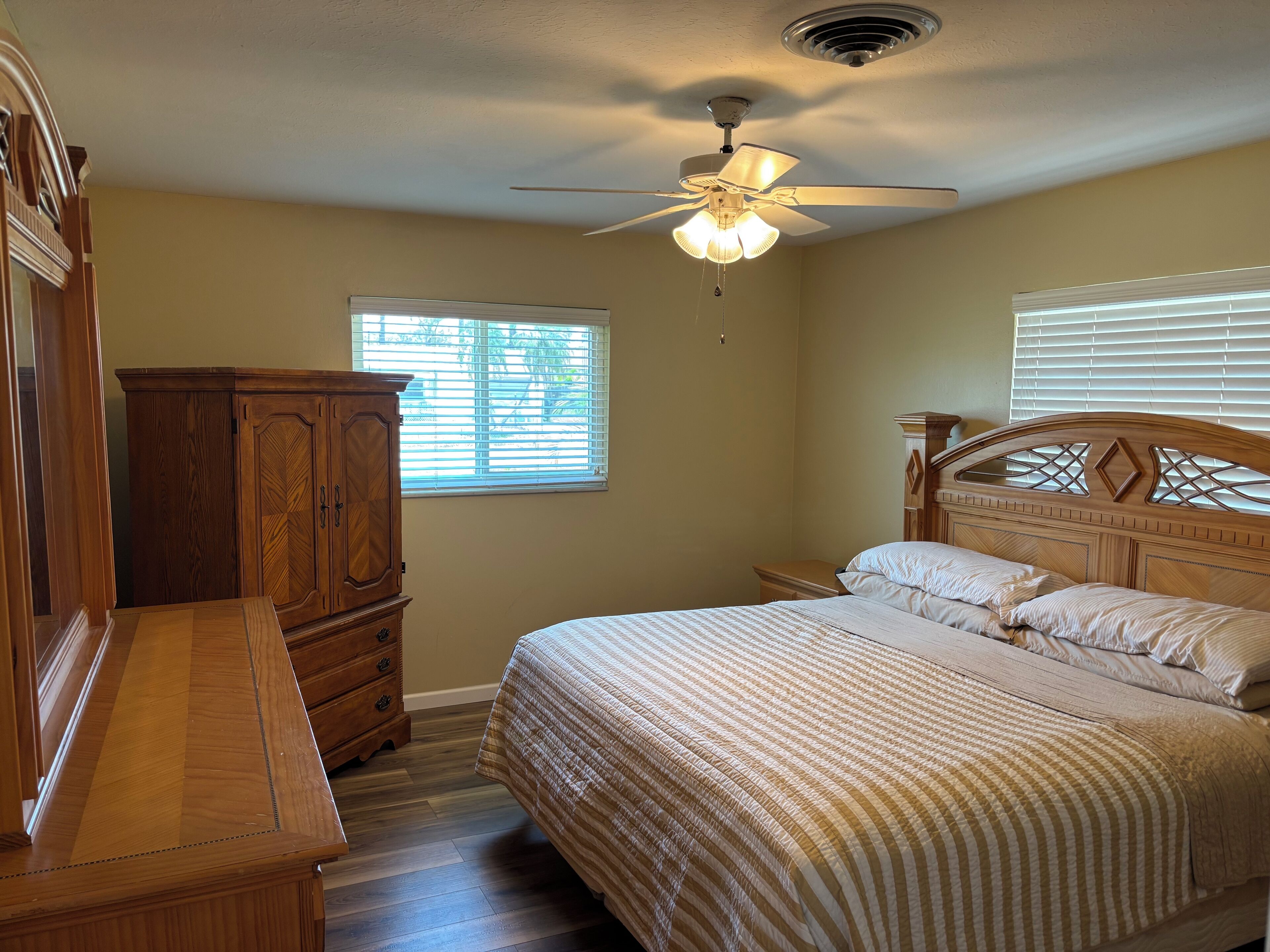 A bedroom with a bed, wooden dresser, and a ceiling fan.