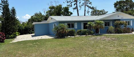 A single-story house with a blue exterior, a gravel driveway, and a well-maintained lawn.