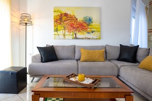 A modern living room with a grey sofa, black and yellow cushions, a wooden coffee table, and a painting of autumn trees.