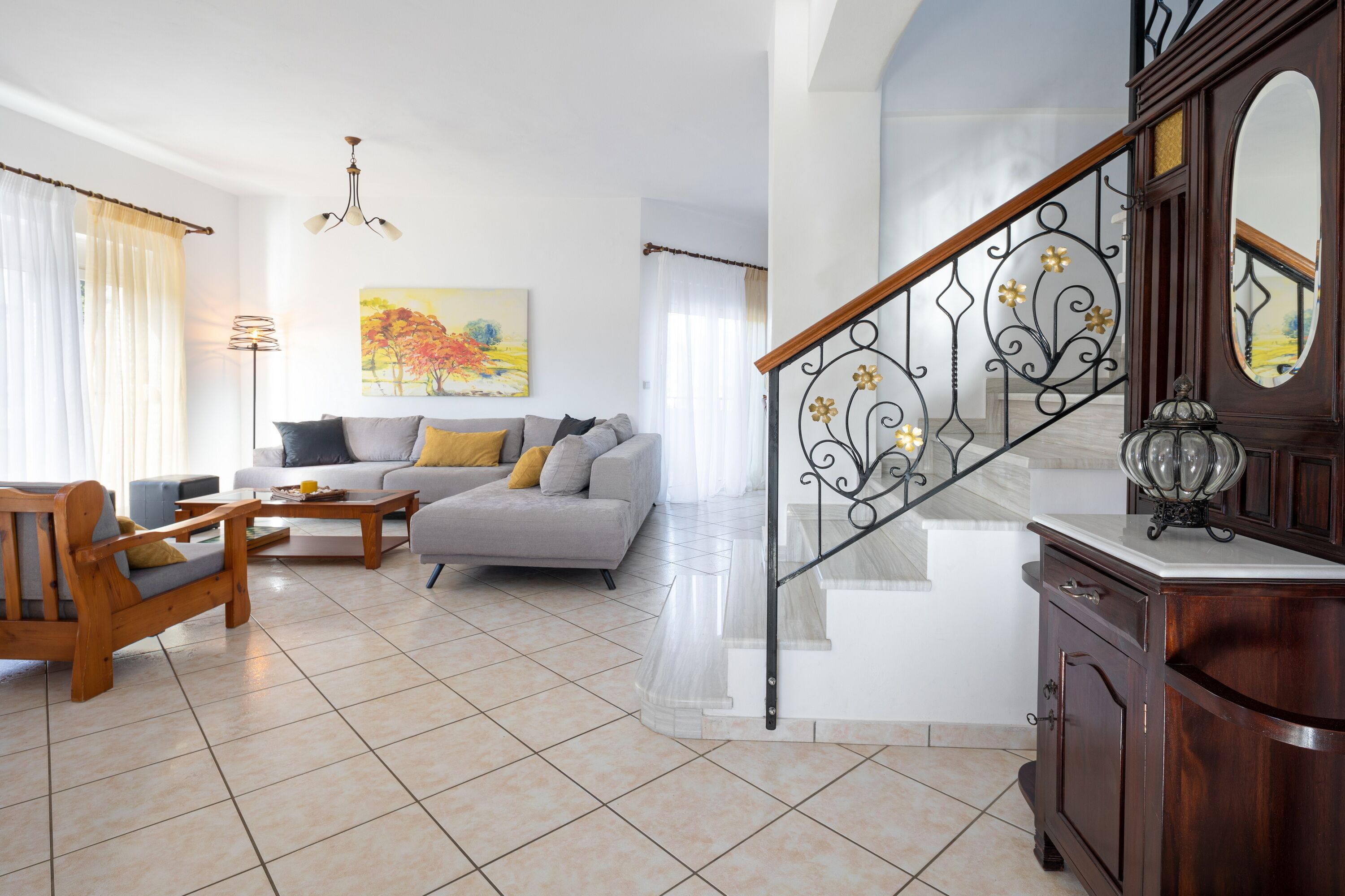 A spacious living room with a sofa, chairs, and a coffee table. A staircase with a decorative railing leads to an upper floor.