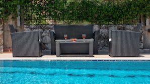 A poolside area with wicker furniture and a table with two glasses of red wine. - Private 4-Bedroom villa, large pool, amazing gardens, relaxing family vacations (Chania)