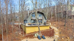 A cabin with a deck, surrounded by a wooded area.