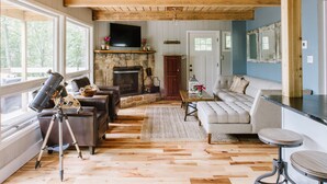 A cozy living room with a stone fireplace, leather furniture, and a large window overlooking greenery.