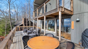 A modern two-story house with a deck, outdoor seating, and large windows.
