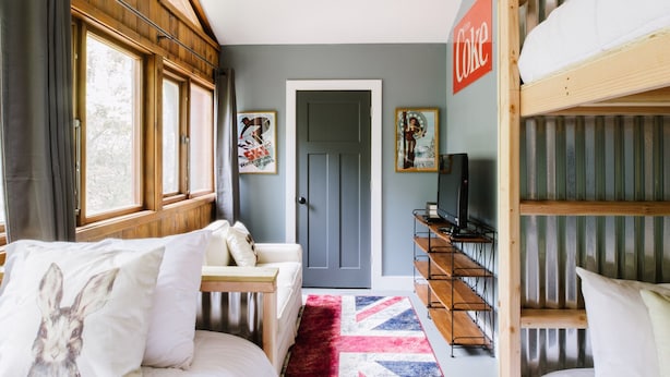 A cozy room with two beds, a wooden desk, a television, and a door leading to another room.