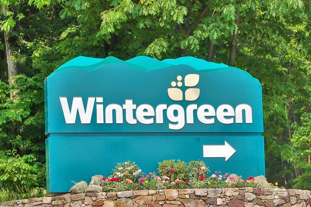 Een Wintergreen bord met een naar rechts wijzende pijl, omringd door groen en bloemen.