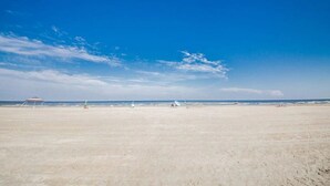 Une vaste plage de sable fin, sous un ciel bleu azur parsemé de quelques nuages.