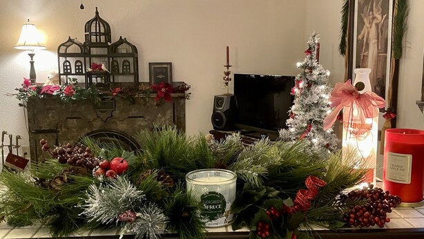 Une cheminée décorée d’un sapin de Noël et d’autres décorations, un téléviseur et une bougie rouge.