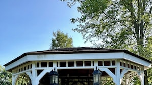 Un belvédère avec un banc et deux lanternes, entouré de verdure.