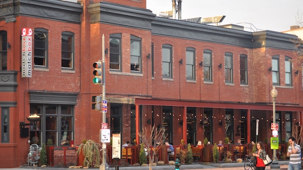 A red brick building with a clock on the facade, outdoor seating, and a green street lamp. - A Cozy-kept Secret  Studio Located In The Heart Of 14/u St/logan Corridors (Washington)