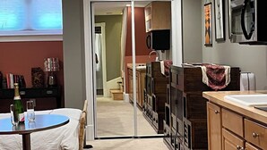 A compact kitchen with wooden cabinets, a countertop, and a microwave. There is a dining area with a table and chairs, and a red couch. - A Cozy-kept Secret  Studio Located In The Heart Of 14/u St/logan Corridors (Washington)