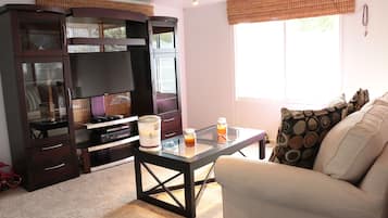 Una sala de estar con un mueble de madera oscura, una mesa de centro de cristal, un sofá blanco y una ventana con vistas al exterior.