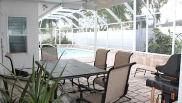 Un patio cubierto con piscina, mobiliario exterior y una parrilla.
