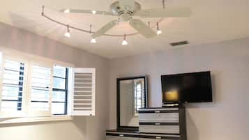 Un dormitorio con ventilador de techo, televisor montado en la pared, cómoda y ventana con persianas.