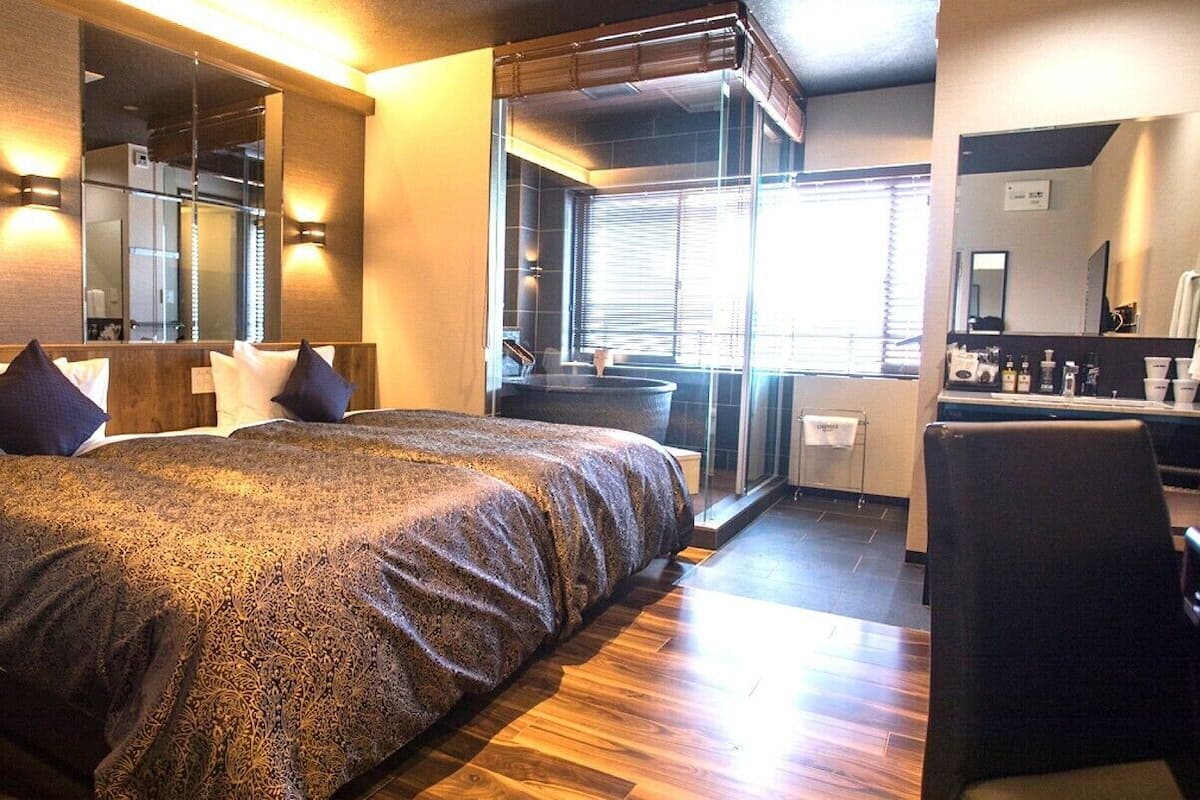 A hotel room with a large bed, a desk, a chair, a bathroom, and a view through a window.