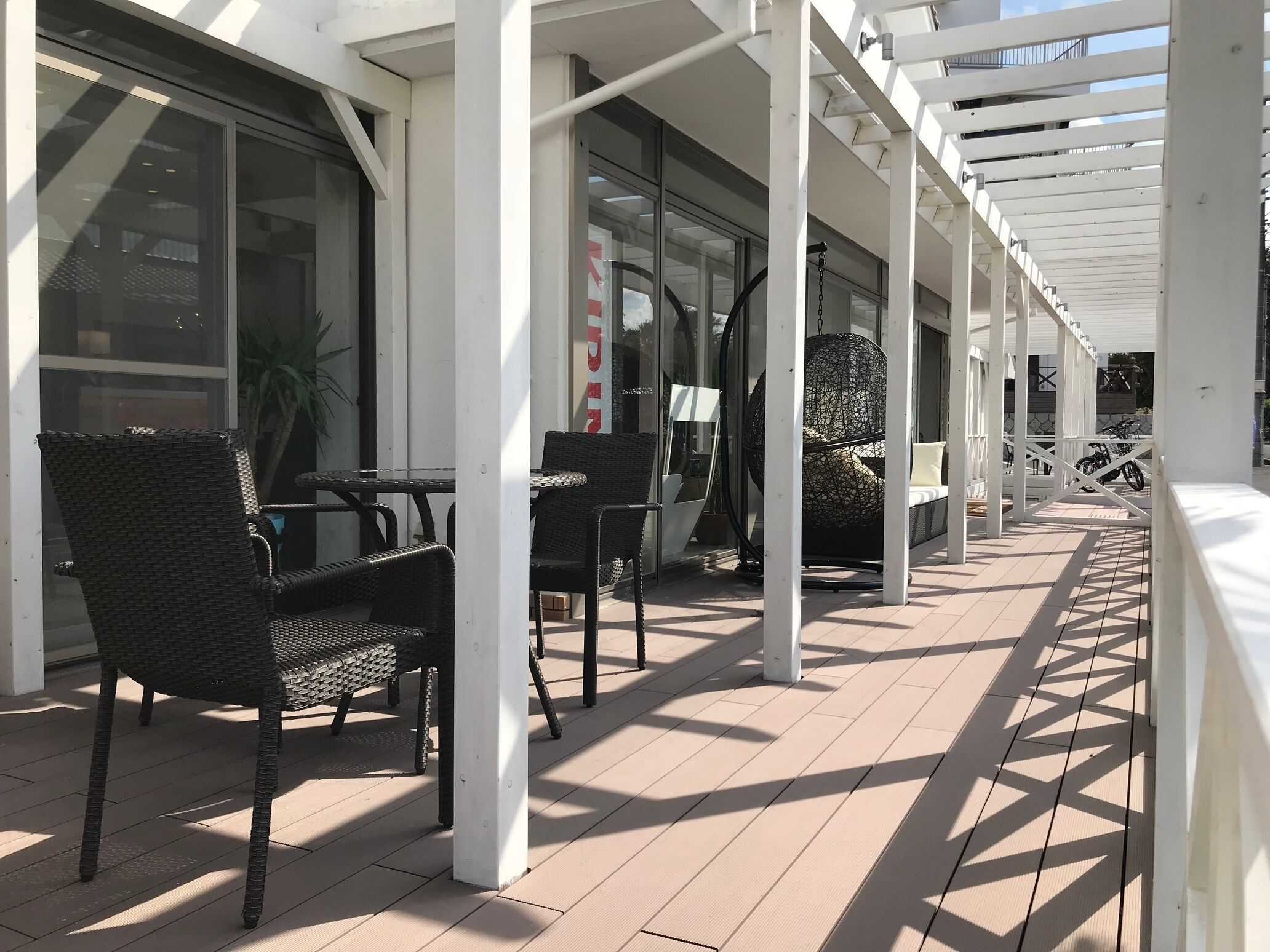 A covered outdoor seating area with wicker chairs and tables, a hanging spherical chair, and a view of the street.