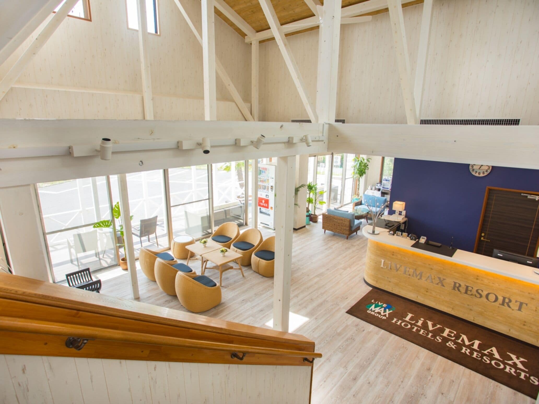 A spacious lobby with high ceilings and large windows, featuring a reception desk, seating area with sofas and chairs, and a visible clock on the wall.