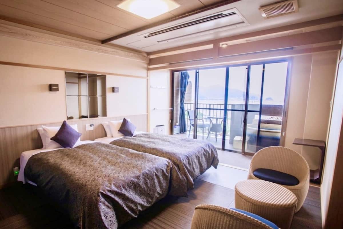 A hotel room with two beds, a balcony with a view, and a seating area.
