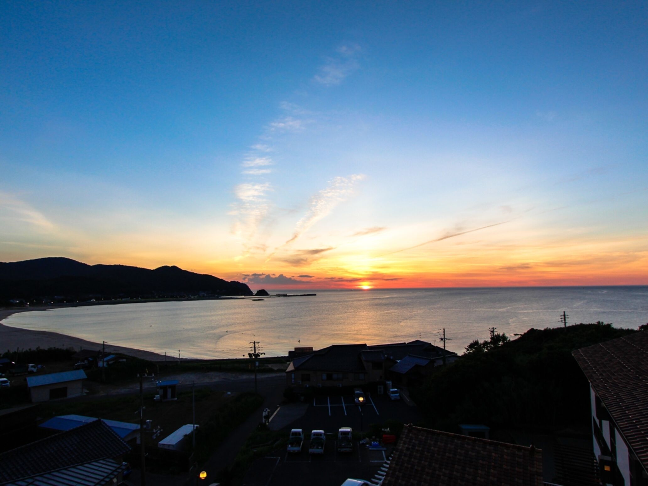 Une vue sur le coucher de soleil sur la côte, avec une plage et des immeubles résidentiels au premier plan.