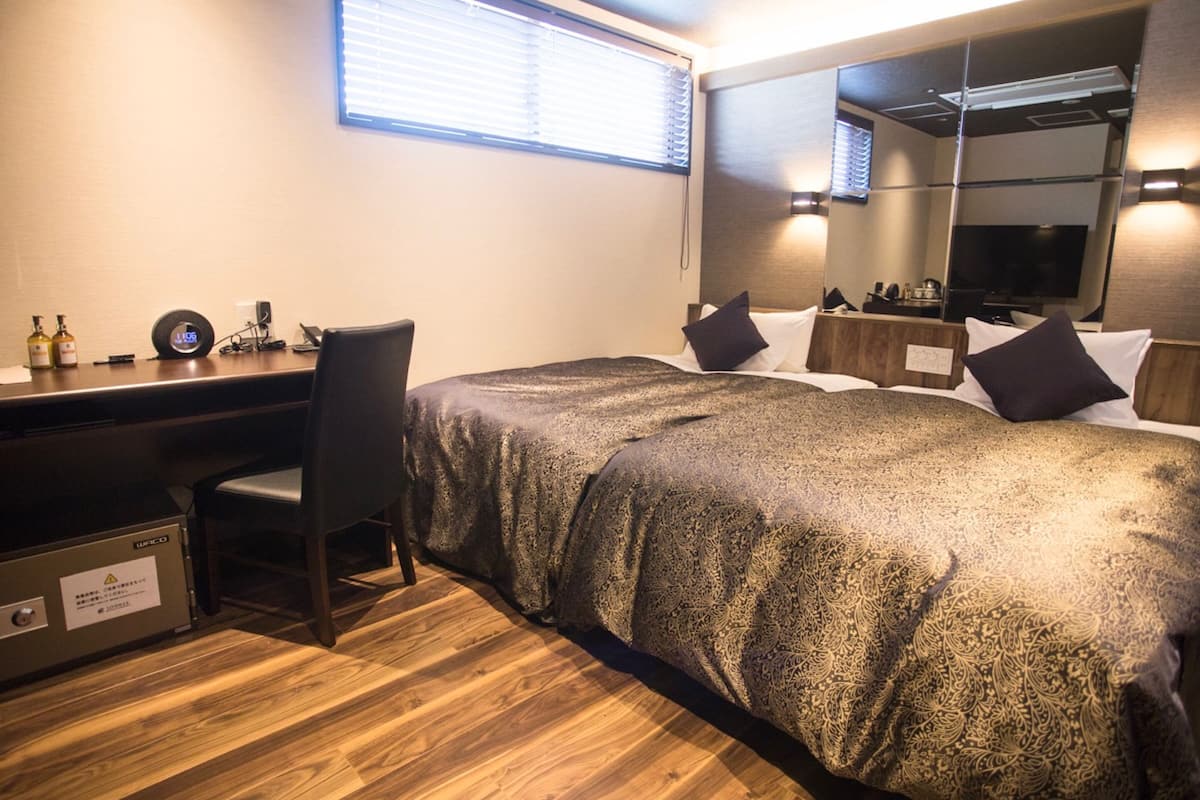 A hotel room with a bed, a desk, a chair, a television, and a mirror.