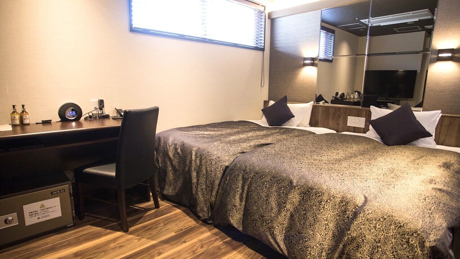 Una habitació d'hotel amb llit, escriptori, cadira, mirall i finestra.
