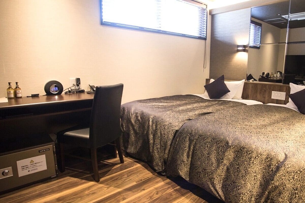 A hotel room with a bed, a desk, a chair, a mirror, and a window.