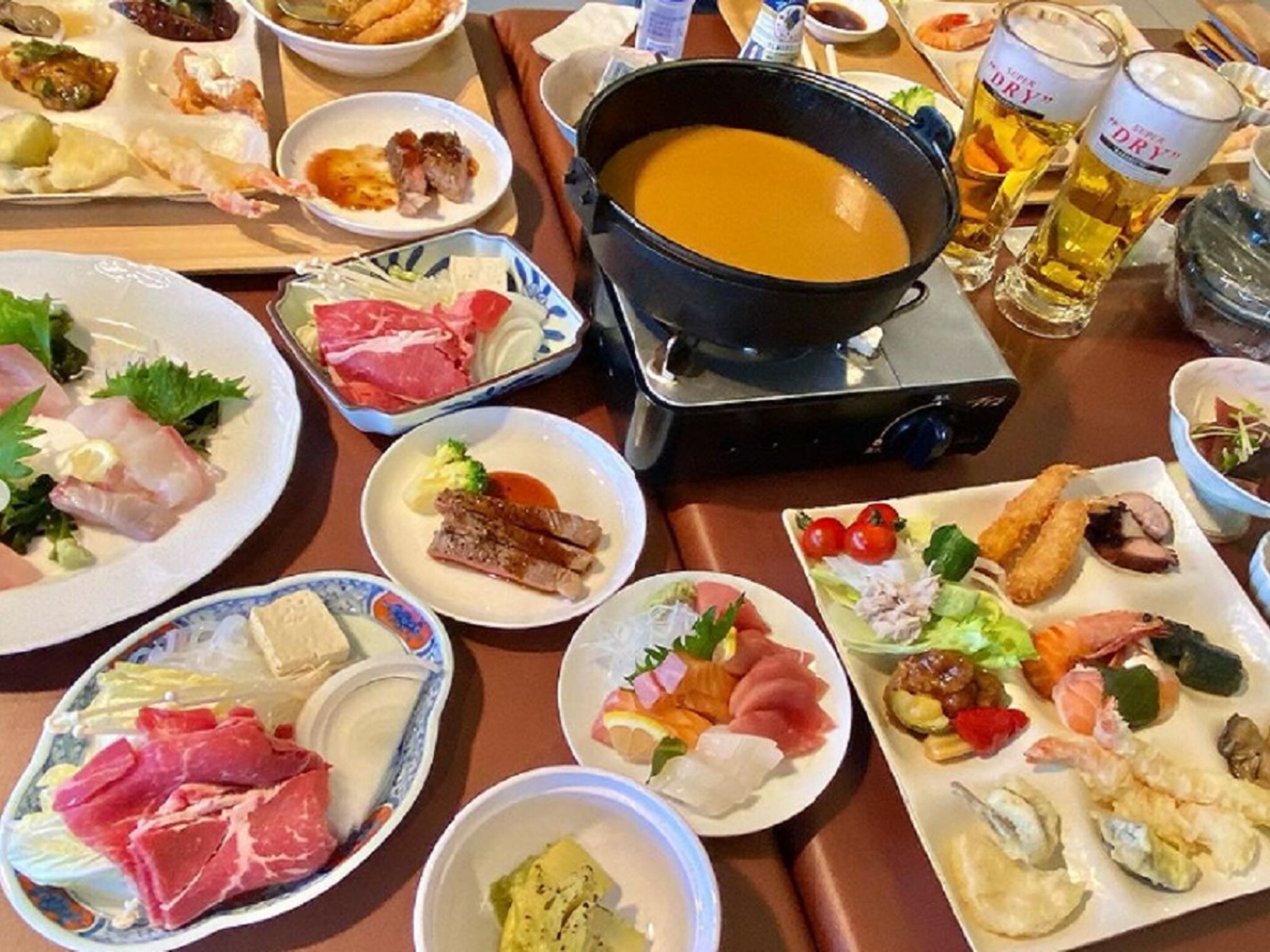 A variety of dishes including sashimi, grilled meats, and a hot pot on a table.