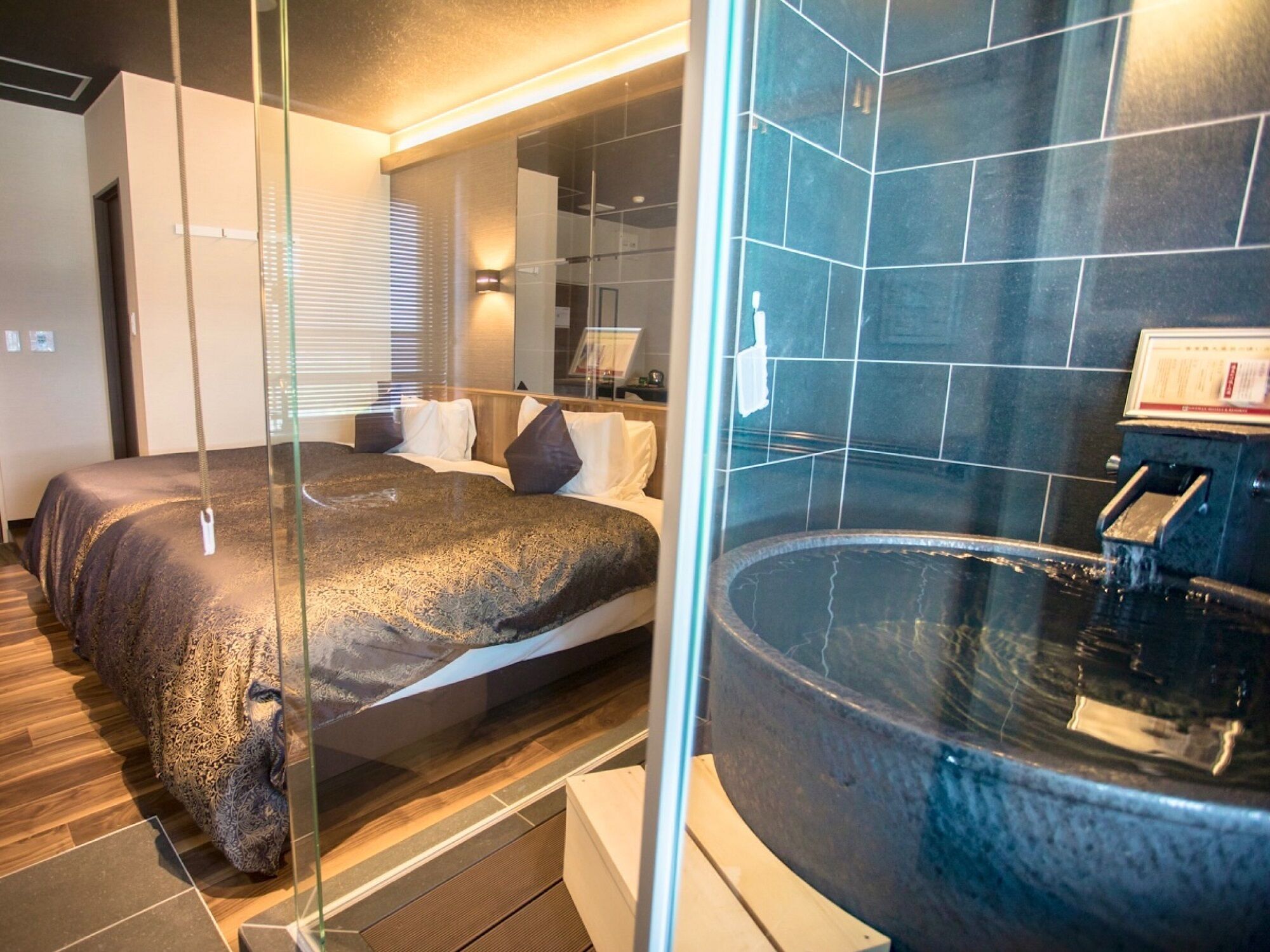 Une chambre d’hôtel moderne dotée d’un grand lit, d’une douche séparée par des parois en verre et d’une baignoire.